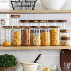 several jars filled with pasta on top of a wooden shelf next to a bowl and glassware