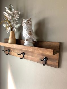 an owl figurine sitting on top of a wooden shelf next to a vase with flowers