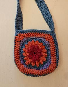 a crocheted bag with an orange flower on the front and blue straps around it