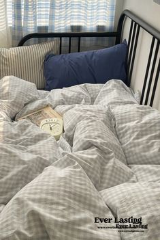 an unmade bed with a book on it in front of a window and curtains