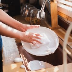 a person washing their hands on a white plate with soapy water in the kitchen