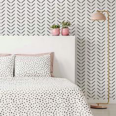 a white bed with black and white wallpaper next to a pink lamp in a bedroom