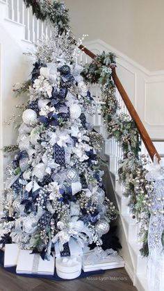 a decorated christmas tree with blue and white decorations on the top, next to stairs