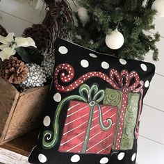 a decorative pillow with a christmas present on it next to a potted pine tree