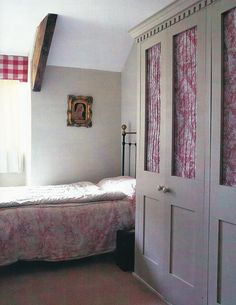 a bed sitting in a bedroom next to a white door and window with pink curtains