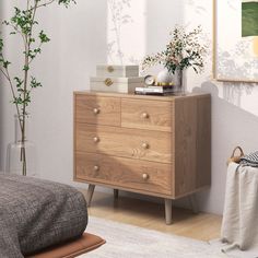 a bedroom scene with focus on the chest of drawers and plants in vases next to it