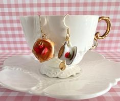 a cup with some earrings on it sitting on a plate next to a pink and white checkered table cloth