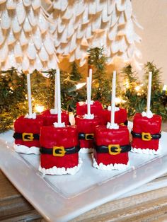 some red cakes with santa hats on them sitting on a white plate next to a christmas tree