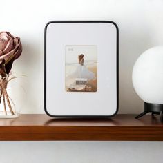 a photo frame sitting on top of a wooden shelf next to a vase with flowers