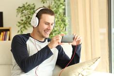 a man sitting on a couch wearing headphones and looking at his cell phone while listening to music