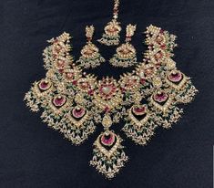 an elaborate necklace and earring set with green, red and white stones on black background