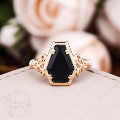 a black stone ring sitting on top of a white box with roses in the background