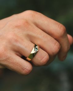 a man's hand wearing a gold ring with a diamond in the middle and a green background