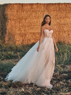 a woman in a wedding dress standing next to a hay bale with her hand on her hip