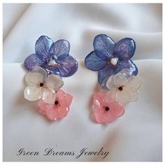 two pink and blue flowers with pearls in them on a white fabric background that has the words green dreams jewelry written below it