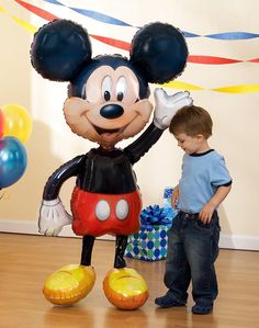 a young boy standing next to a mickey mouse balloon