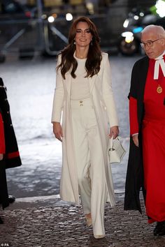 a woman in white is walking with an older man and she has a red coat over her shoulders