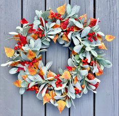 a wreath with leaves and berries is hanging on a wall next to a wooden fence