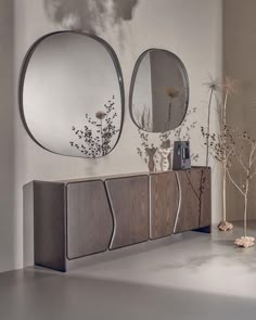 two round mirrors are hanging on the wall above a dresser with flowers in vases