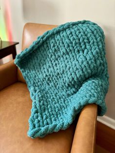 a blue crocheted blanket sitting on top of a brown leather chair