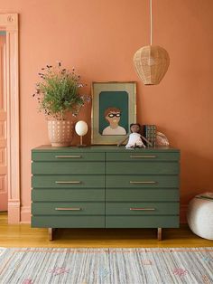 a green dresser sitting in front of a pink wall with pictures and plants on it