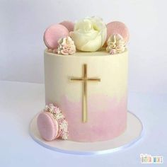 a pink and white cake with a cross on the top is decorated with flowers, cookies and other decorations