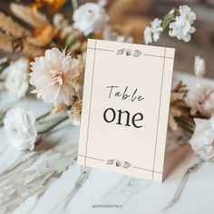 there is a sign that says table one on it next to some white and pink flowers