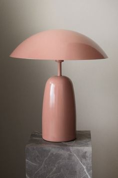 a pink table lamp sitting on top of a marble block next to a gray wall