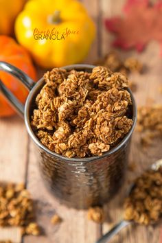 a metal cup filled with granola sitting on top of a wooden table next to oranges