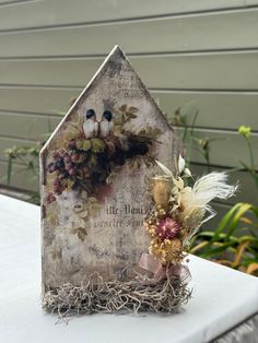 a birdhouse with two birds sitting on top of it's roof next to flowers