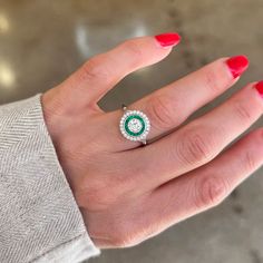 a woman's hand with red nails and a green ring on her left hand