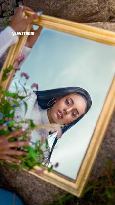 a woman is looking at her reflection in a mirror while she holds the frame over her head