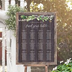 a wooden sign with greenery on it and the names of each wedding ceremony table