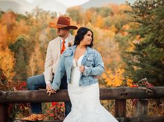 a man and woman standing next to each other on a wooden fence with trees in the background