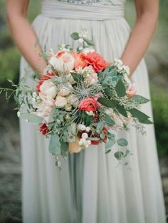 a bride holding a bouquet of flowers and greenery in her hands, wearing a wedding dress