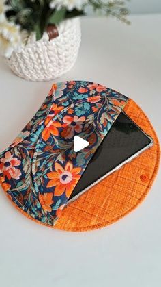 a cell phone sitting on top of an orange and blue flowered coaster next to a white potted plant