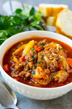 a white bowl filled with meat and vegetable soup next to bread on a table top