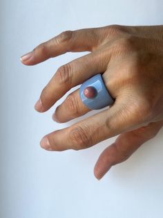 a person's hand with a blue ring on top of their finger and an object in the middle