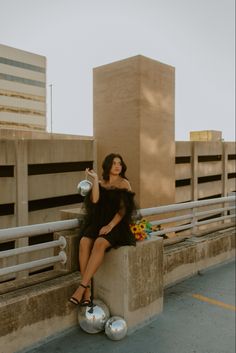 a woman in a black dress is sitting on a cement block with her legs crossed