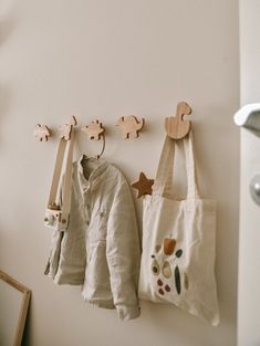 three wooden pegs are hanging on the wall next to two bags and coat hooks