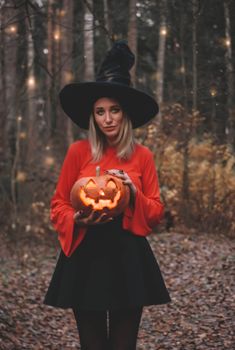 a woman in a witches hat holding a pumpkin