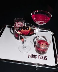 two martinis on a tray with red wine and blackberries in the glass next to each other