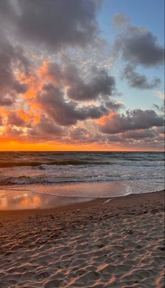 the sun is setting over the ocean with clouds in the sky and sand on the beach