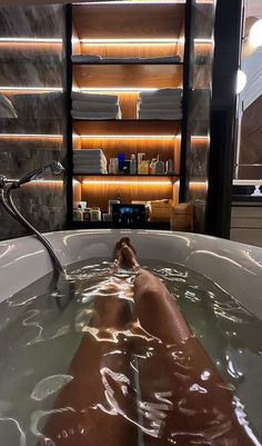 a person laying in a large bathtub filled with water next to a book shelf