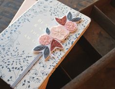 an open book with flowers on it sitting on top of a wooden table next to a box