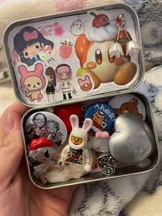 someone is holding an open tin with various items in it and there are other things inside the tin