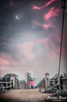 a person standing on a walkway under a cloudy sky with the moon in the distance