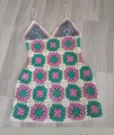 a crocheted dress with pink, green and white flowers on it sitting on the floor