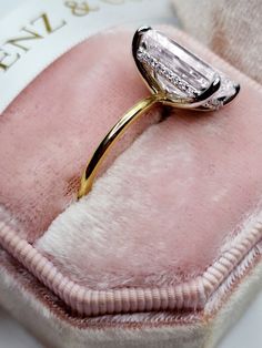 a diamond ring sitting on top of a pink velvet cushion in a white and gold box