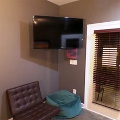 a tv mounted to the wall in a living room next to a brown leather chair